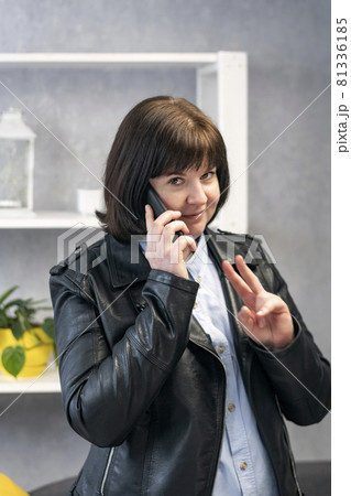 Young woman in leather jacket is talking on phone and asks to wait two minutes. Business lady decides work issues. Young woman in leather jacket is talking on phone and asks to wait two minutes. Business lady decides work issues. 81336185