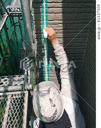 戸建住宅の外壁塗り替え塗装前にサイディング目地シーリング補修を行う男性塗装職人 81337509