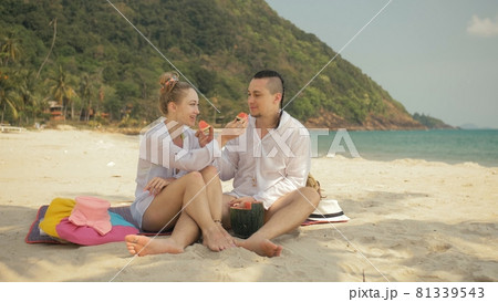 The cheerful love couple holding and eating slices of watermelon on tropical sand beach sea. Romantic lovers two people spend summer weekend. 81339543