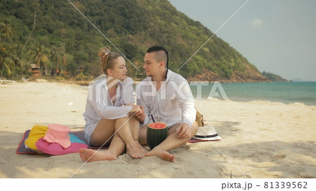 The cheerful love couple holding and eating slices of watermelon on tropical sand beach sea. Romantic lovers two people spend summer weekend. 81339562