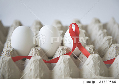 White eggs in an egg carton with a red awareness ribbon on a white background. 81339586