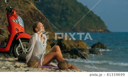 Scooter road trip. Woman alone on red motorbike in white clothes on sand beach by ocean. One girl caucasian tourist walk near tropical palm tree. Scooter road trip. Woman alone on red motorbike in white clothes on sand beach by ocean. One girl caucasian tourist walk near tropical palm tree. 81339699