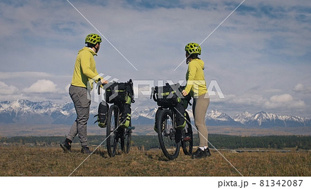 The man and woman travel on mixed terrain cycle touring with bikepacking. The two people journey with bicycle bags. Mountain snow capped. 81342087