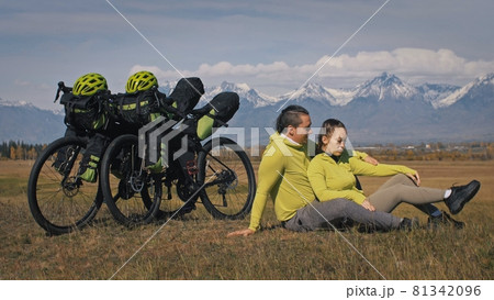 The man and woman travel on mixed terrain cycle touring with bikepacking. The two people journey with bicycle bags. Mountain snow capped. The man and woman travel on mixed terrain cycle touring with bikepacking. The two people journey with bicycle bags. Mountain snow capped. 81342096