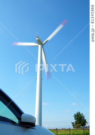 自動車のボンネットの向こうで風力発電の風車が快晴の青空に向かって高く聳え立っている構図 81345966