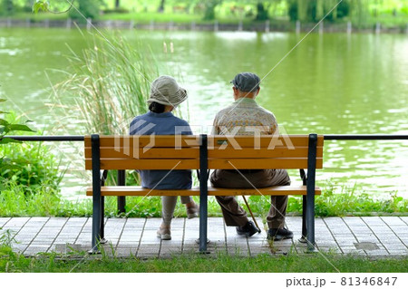 池のほとりのベンチに座る老夫婦 81346847
