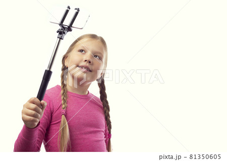 Cute little caucasian girl taking a photo using a modern smartphone on a white background. Selfie stick Cute little caucasian girl taking a photo using a modern smartphone on a white background. Selfie stick 81350605
