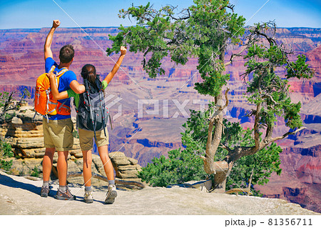 Grand Canyon hikers tourists couple cheering success with arms up happy for hike achievement. Backpackers hiking with backpacks standing at view of famous american landmark, USA trip travel 81356711