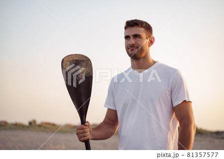 Young fit man standing on the beach and holding paddle 81357577