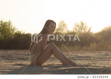 Feminine young topless woman sunbathing on sandy shore at sundown Feminine young topless woman sunbathing on sandy shore at sundown 81358349
