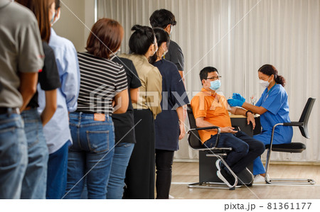 Citizens of different ages in a row standing and waiting for a vaccine injection while medical people injecting to senior man in face mask. Covid-19 or coronavirus vaccination concept Citizens of different ages in a row standing and waiting for a vaccine injection while medical people injecting to senior man in face mask. Covid-19 or coronavirus vaccination concept 81361177