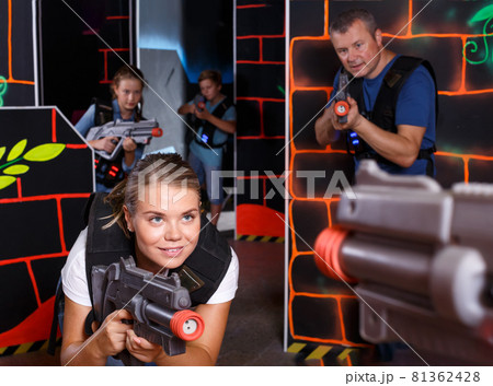 Smiling female aiming laser gun at other players during laser tag game 81362428