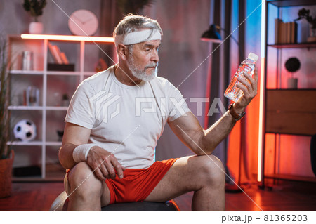 Senior man sitting on fitball with bottle of water in hand Senior man sitting on fitball with bottle of water in hand 81365203