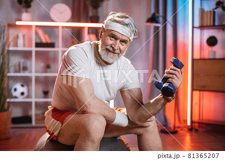 Old man sitting on swiss ball and training with dumbbells 81365207