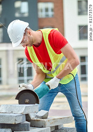 Concentrated worker in a hardhat and goggles leaning over construction materials 81373579