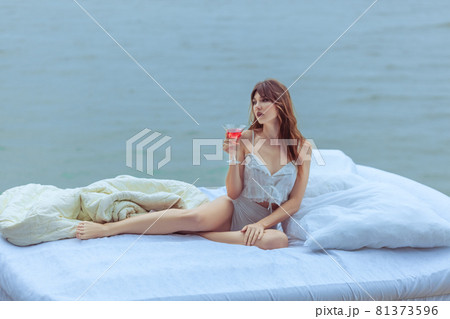 Woman with a glass of wine on a bed in the ocean. Woman with a glass of wine on a bed in the ocean. 81373596