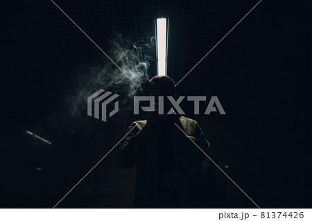 Portrait of young caucasian man smoking e-cigarette in dark with line light 81374426