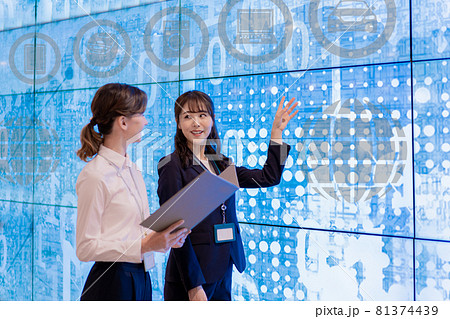 展示場で画面の説明をする女性スタッフ2名 81374439