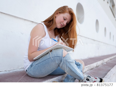 teenage girl draws in the sketchbook while sitting on the steps 81375177
