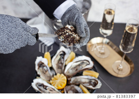Hands of waiter in special gloves opening an oyster Hands of waiter in special gloves opening an oyster 81383397