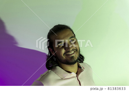 Studio portrait with colored lights purple and green of a latino man with piercings and beard looking at camera 81383633