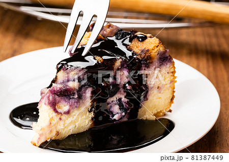 Using metal fork taking a bite from a piece of homemade blueberry and crumble cheesecake topping with chocolate. 81387449