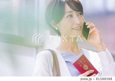パスポート持ってスマホで通話している女性 81388388