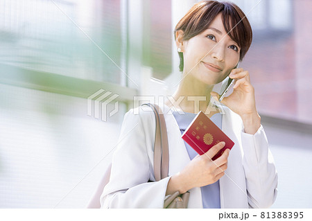 パスポート持ってスマホで通話している女性 81388395