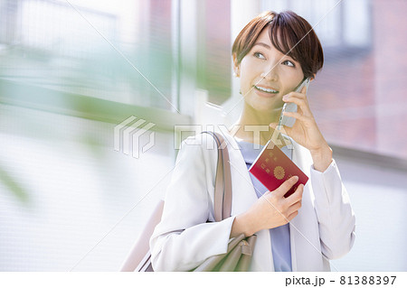 パスポート持ってスマホで通話している女性 81388397