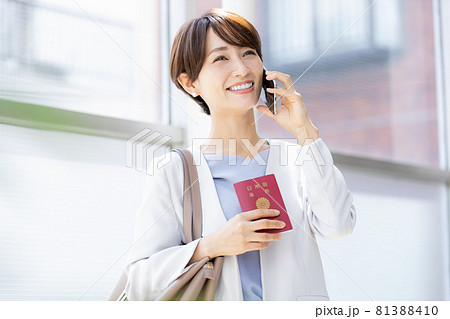 パスポート持ってスマホで通話している女性 81388410
