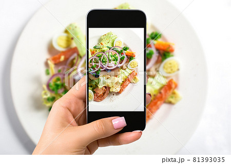 Photographing food concept - woman takes picture of fresh salad with lettuce, eggs, tomatoes, onion rings, peppers 81393035