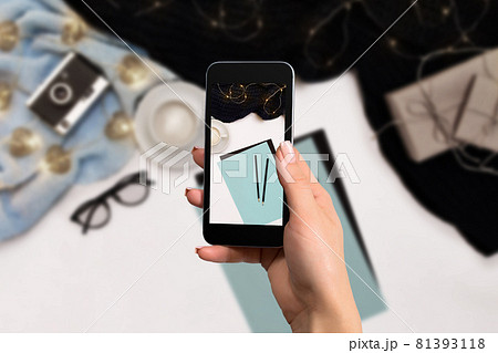 Female hand with a smartphone makes a photo workspace with notebook, coffee cup, scarf, glasses. 81393118