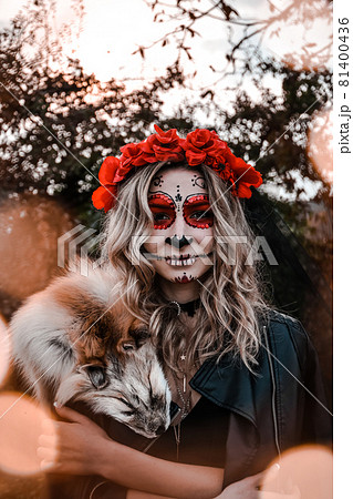 Happy Halloween concept. Scared horrible female sitting in special outfit, wears white clay skull, professional sugar skull makeup to look spooky, wears black clothes playing with fox fur Happy Halloween concept. Scared horrible female sitting in special outfit, wears white clay skull, professional sugar skull makeup to look spooky, wears black clothes playing with fox fur 81400436