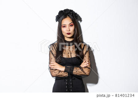 Skeptical and unamused asian woman dressed in halloween costume looking disappointed at camera, cross arms chest. Female in black gothic dress and wreath judging someone Skeptical and unamused asian woman dressed in halloween costume looking disappointed at camera, cross arms chest. Female in black gothic dress and wreath judging someone 81401234