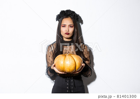 Image of grimacing asian woman in witch costume hate carve pumpkin for halloween, looking disappointed, standing over white background Image of grimacing asian woman in witch costume hate carve pumpkin for halloween, looking disappointed, standing over white background 81401300