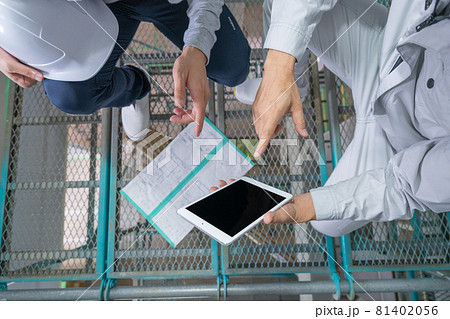 一戸建ての建築現場 2階の足場からタブレットを見て確認する男性2人の手元のアップ 81402056