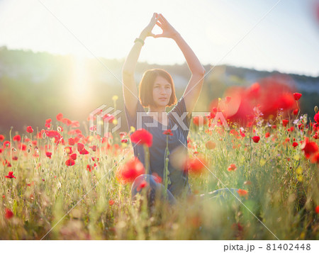 A beautiful woman meditates on a poppy field at sunset A beautiful woman meditates on a poppy field at sunset 81402448