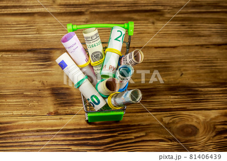 Shopping cart with money from different countries: euros, us dollars, ukrainian hryvnia, russian rubles, egyptian pounds on wooden background 81406439