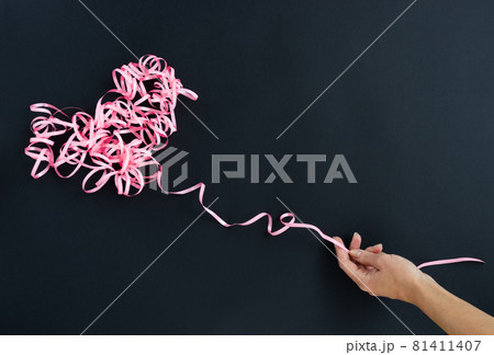 Female hand holding pink curly ribbon heart. Serpentine heart. Female hand holding pink curly ribbon heart. Serpentine heart. 81411407