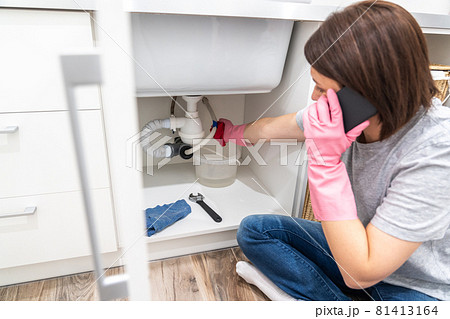 Woman sitting near leaking sink in laundry room calling for help Woman sitting near leaking sink in laundry room calling for help 81413164