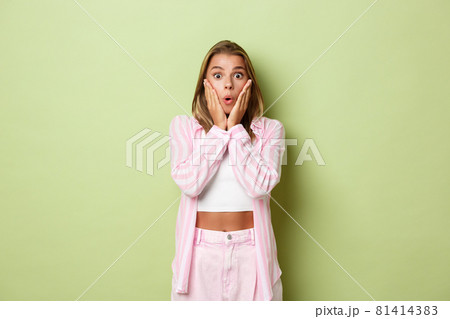 Portrait of attractive blond female model in pink outfit, looking surprised, gasping and staring at promo, standing over green background Portrait of attractive blond female model in pink outfit, looking surprised, gasping and staring at promo, standing over green background 81414383