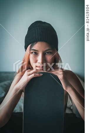 portrait of Asian girl with street fashion holding a skateboard on a sofa indoor. portrait of Asian girl with street fashion holding a skateboard on a sofa indoor. 81419304