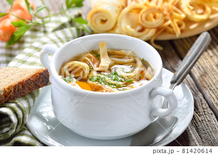 Delicious homemade beef broth with pancake strips, served with bread on a wooden table 81420614