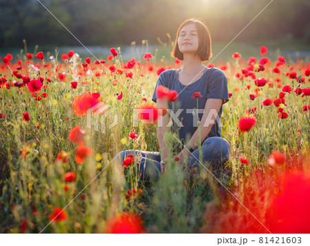 A beautiful woman meditates on a poppy field at sunset A beautiful woman meditates on a poppy field at sunset 81421603