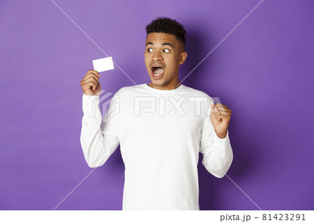 Impressed african-american guy, looking at credit card with amazement, standing over purple background 81423291
