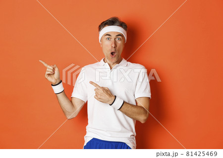 Portrait of surprised middle-aged man doing sports, showing something amazing, pointing fingers left and looking fascinated, wearing activewear for workout, standing over white background Portrait of surprised middle-aged man doing sports, showing something amazing, pointing fingers left and looking fascinated, wearing activewear for workout, standing over white background 81425469