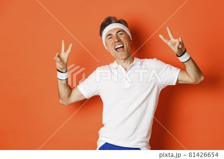 Image of happy and healthy middle-aged man in sport clothing, showing peace signs and smiling, workout over orange background Image of happy and healthy middle-aged man in sport clothing, showing peace signs and smiling, workout over orange background 81426654