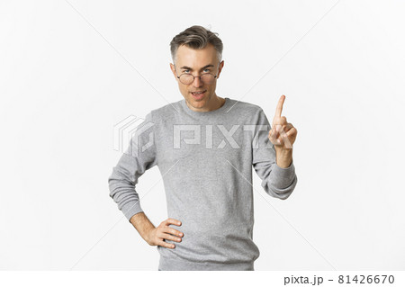 Image of handsome middle-aged man in glasses and grey sweater, showing one finger, teaching a lesson, standing over white background Image of handsome middle-aged man in glasses and grey sweater, showing one finger, teaching a lesson, standing over white background 81426670