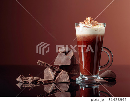 Hot chocolate with whipped cream and pieces of dark chocolate on a brown background. Hot chocolate with whipped cream and pieces of dark chocolate on a brown background. 81428945