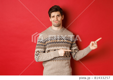 Concept of christmas celebration, winter holidays and lifestyle. Image of skeptical and displeased handsome man in xmas sweater, pointing fingers right and do not recommend product Concept of christmas celebration, winter holidays and lifestyle. Image of skeptical and displeased handsome man in xmas sweater, pointing fingers right and do not recommend product 81433257